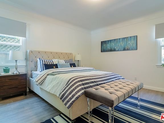 Bedroom with queen bed, bench, rug, nightstand, and windows.