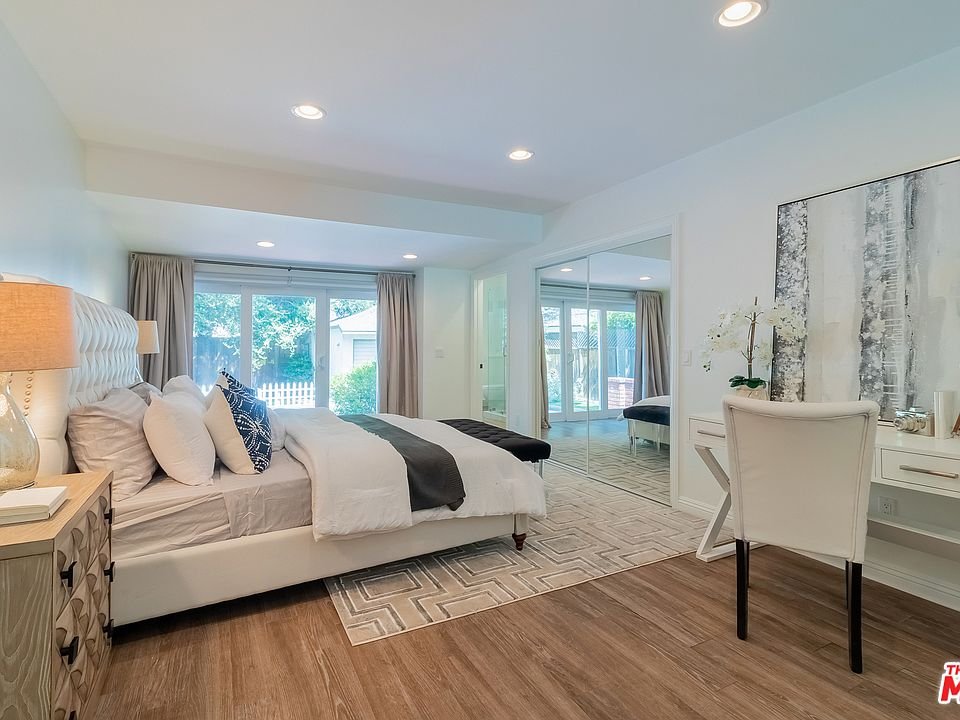 Bedroom with bed, pillows, nightstand, chair, desk, and windows.
