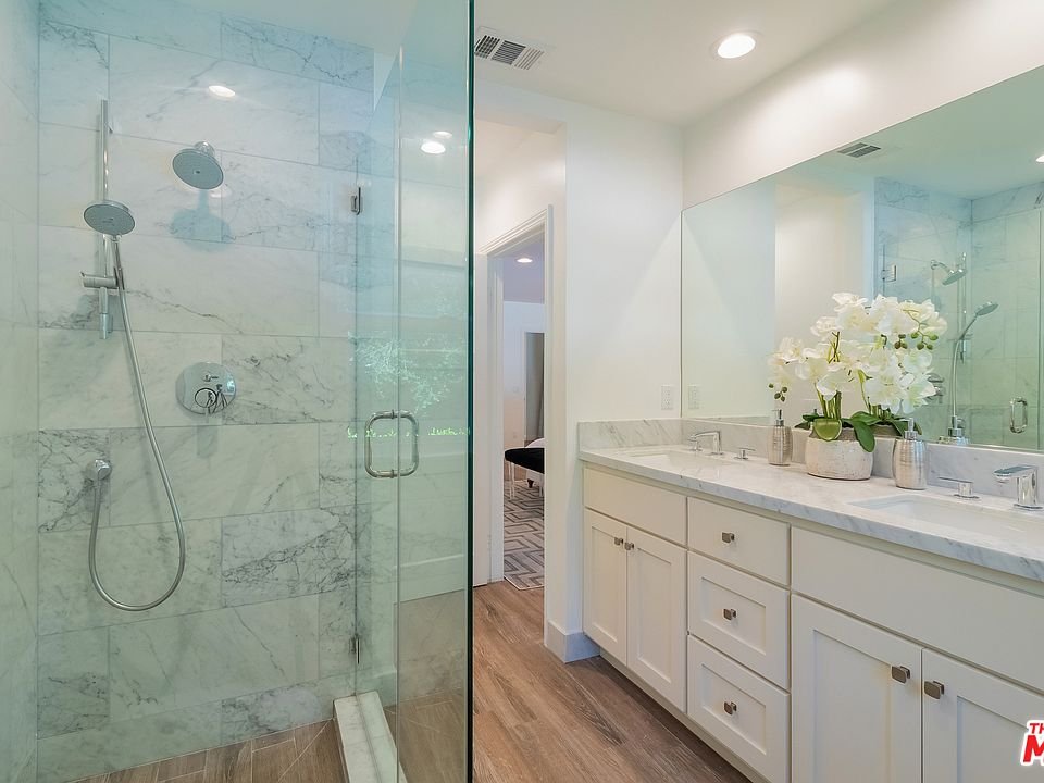 Bathroom with glass shower, marble tiles, double sink vanity, and orchids.