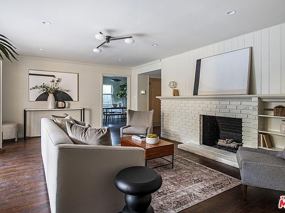 Living room with white brick fireplace, gray sofa, throw pillows, wooden floor, coffee table, accent chair, and houseplants