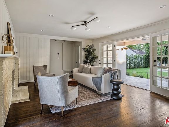 Living room with light sofa, gray armchairs, wooden coffee table, French doors, white walls, and decorative fireplace