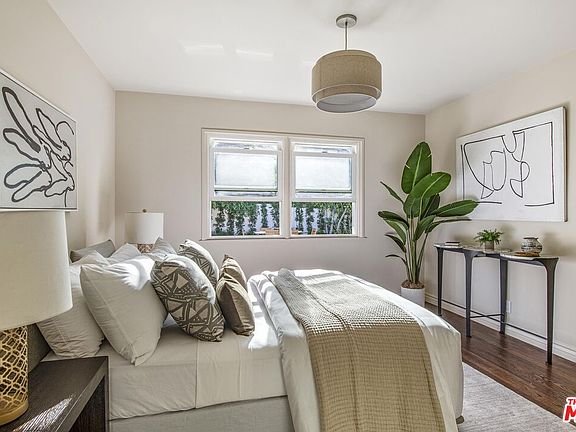 Bedroom with bed, decorative pillows, textured blanket, windows, plant, and wall artwork
