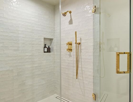 Shower with white tiles, glass enclosure, golden showerhead, and alcove for toiletries