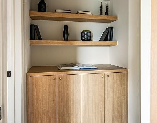 Shelving unit with wooden shelves, books, decorative vases, and light wood cabinet