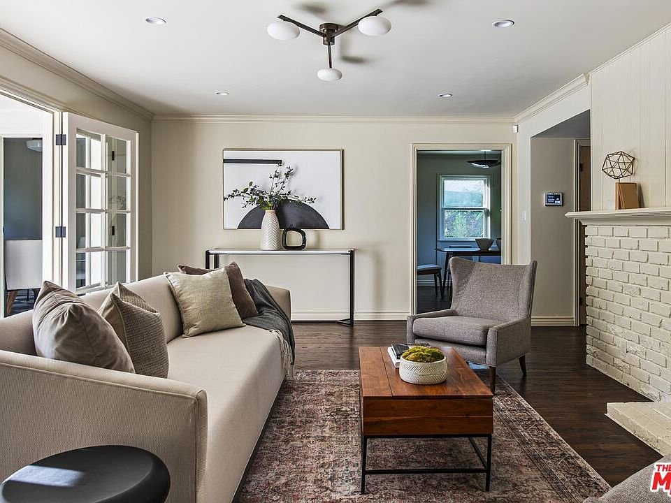 Living room with light sofa, decorative pillows, wooden coffee table with plant, neutral rug, wall artwork, and doorways to other rooms