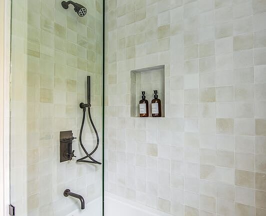 Shower with glass door, tiled walls, showerhead, and built-in soap niche
