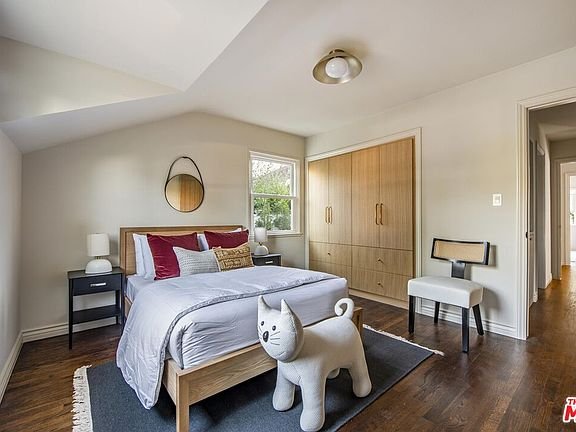 Bedroom with wooden bed, gray bedding, nightstand with round mirror, cat-shaped stool, and wardrobe
