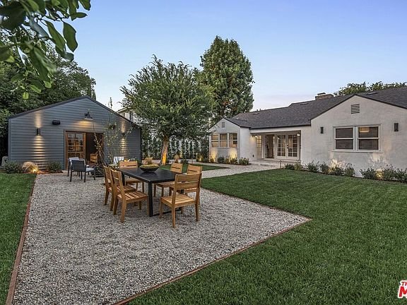 California real estate home backyard with dining table, chairs, grass, landscaping, and house with gray shed