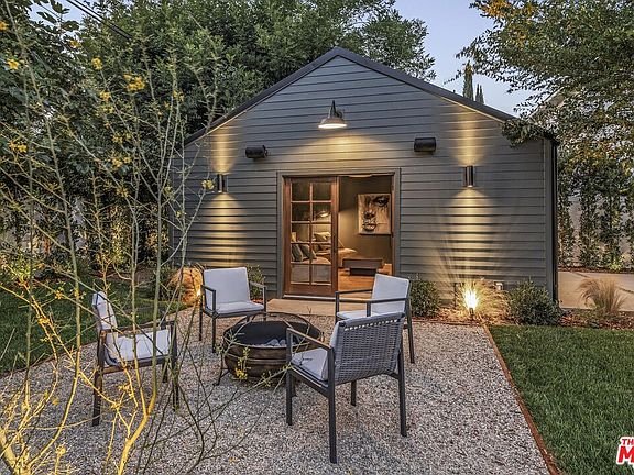 California real estate home with small gray house, fire pit, chairs, and green landscaping