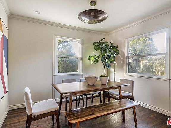 Dining room with wooden table, chairs, bench, potted plant, and large windows