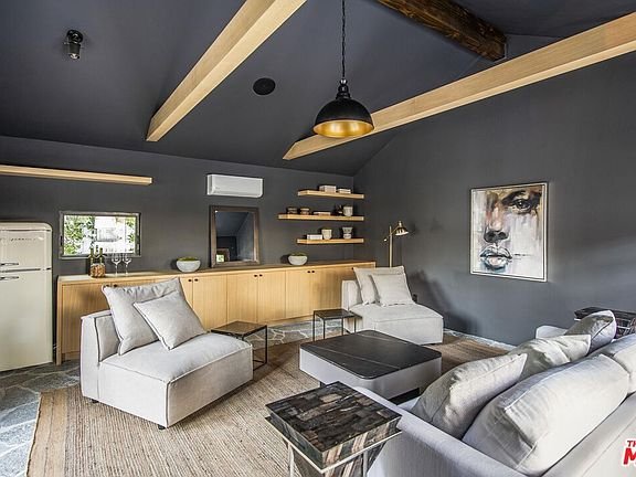 Living room with dark gray wall, wooden beams, white sofas, black coffee table, face artwork, and shelves with decor