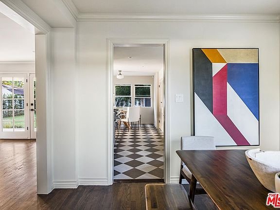 Interior with wooden dining table, hallway with geometric painting, and checkered floor in another room
