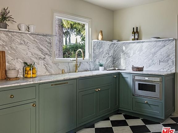 Kitchen with green cabinets, marble countertop and backsplash, checkered floor, window, microwave, and countertop decor