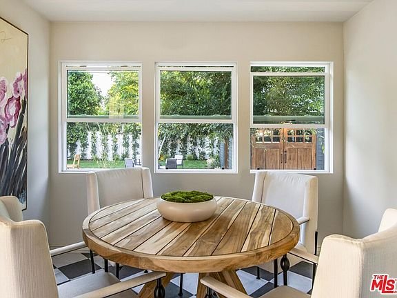 Dining area with round wooden table, four white chairs, windows, and decorative bowl with plants