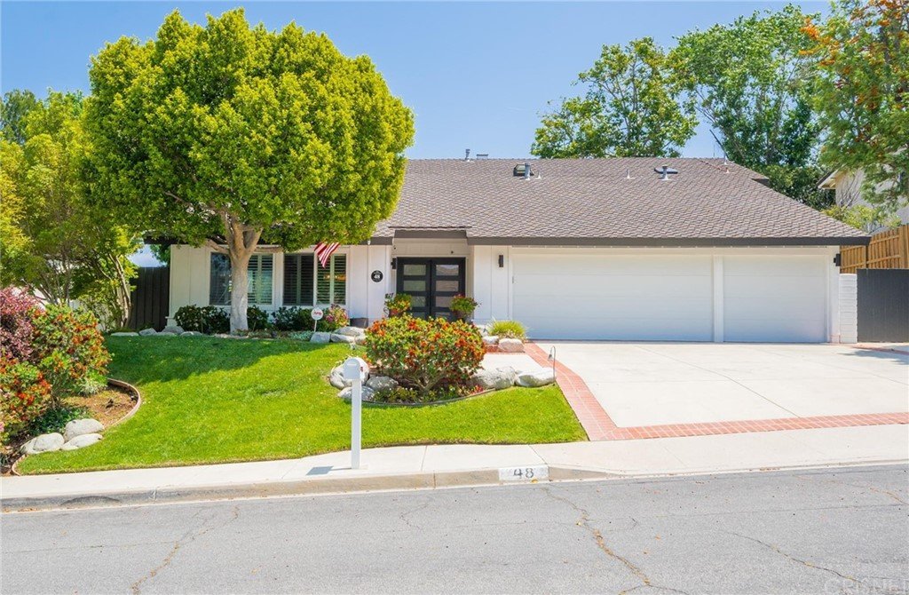 California real estate house with front yard, large tree, shrubs, flowers, sloped roof, and garage.