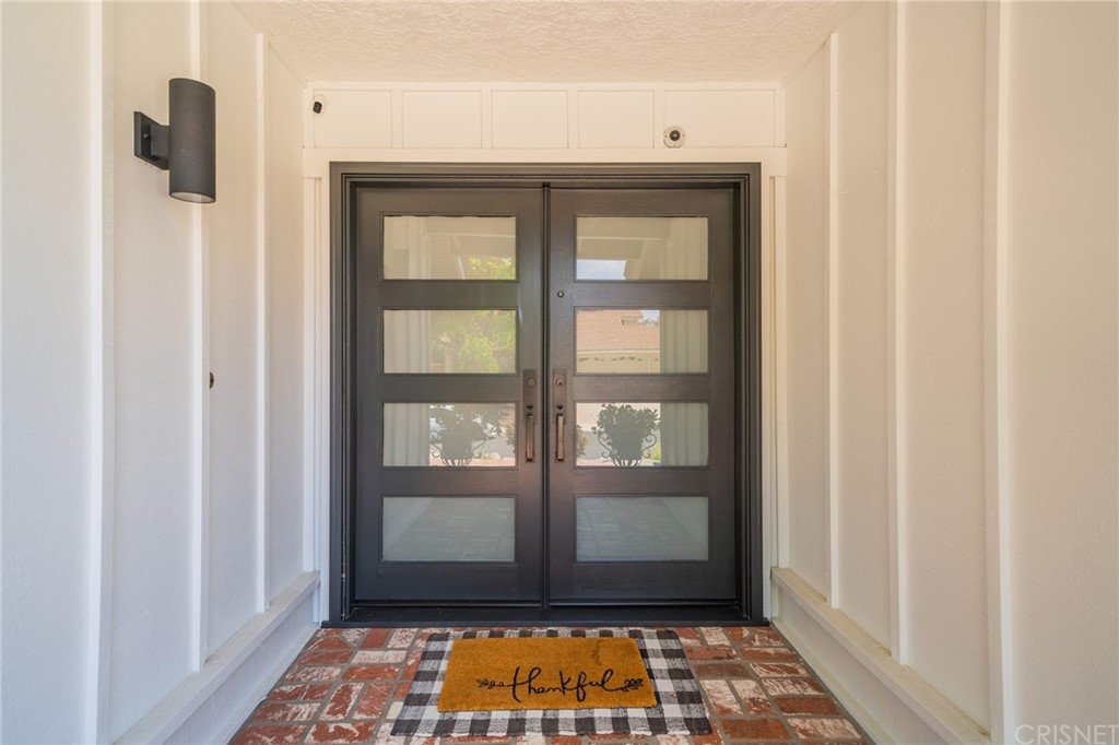 Real estate house front entrance with glass double doors, welcome mat, and tile floor.