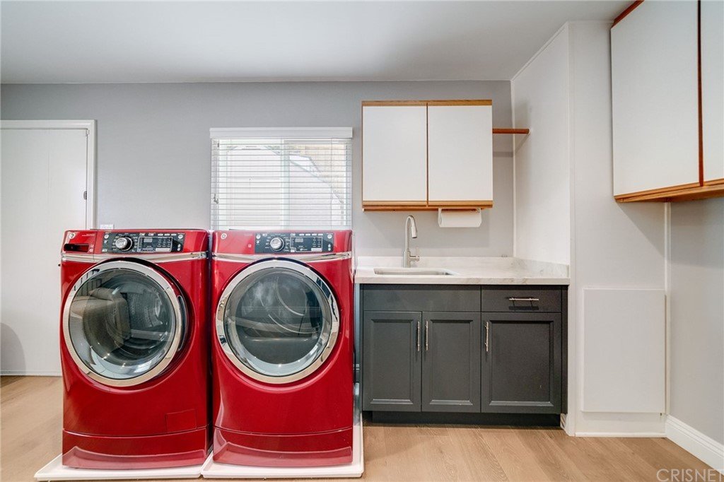 Laundry room with washer, dryer, sink, gray walls, and white cabinets.