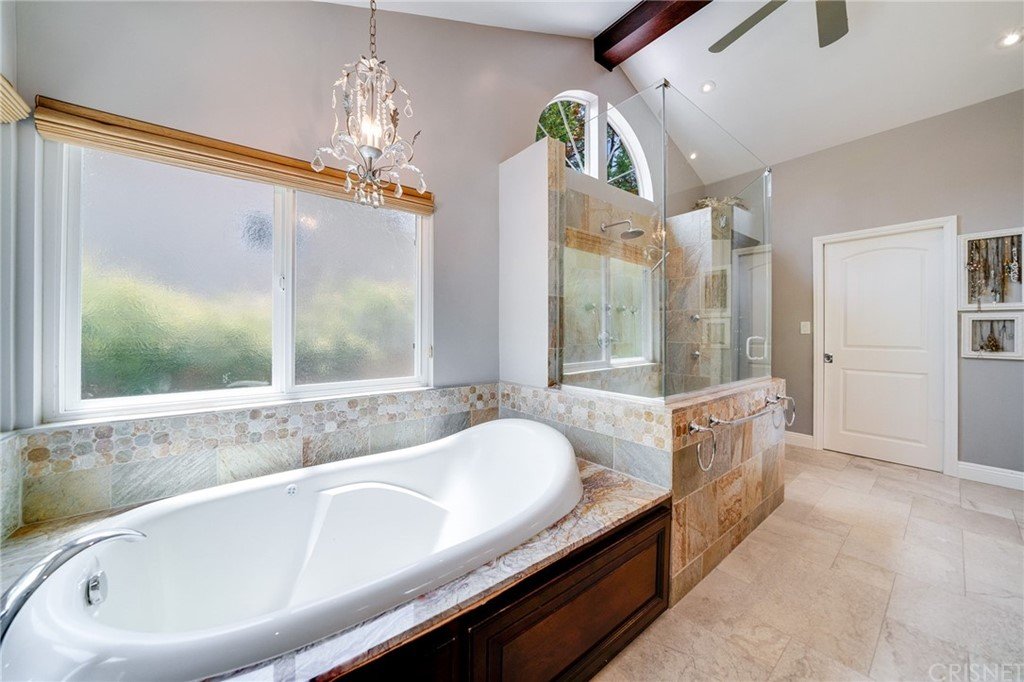 Bathroom with bath tub, glass shower, windows, stone tiles, and lights.