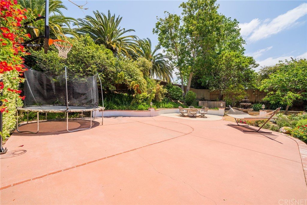 California real estate house backyard with trampoline, basketball hoop, palm trees, and seating area.