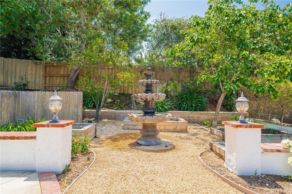Garden with stone fountain, gravel path, plants, and small lights.