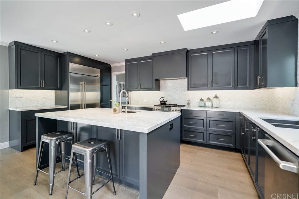 Kitchen with dark cabinets, marble counter, island, stainless steel appliances, and ceiling lights.