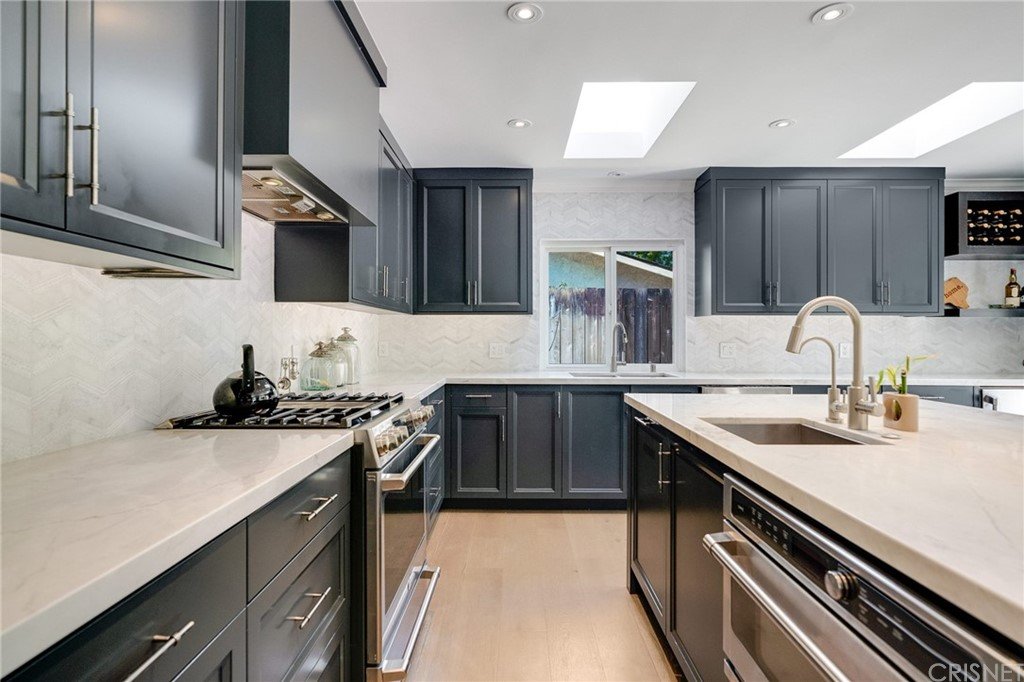 Kitchen with dark cabinets, white counter, stainless steel appliances, and window light.