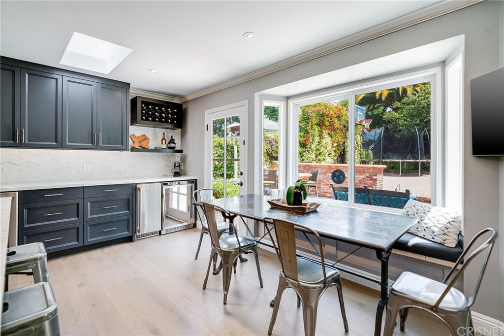 Kitchen with dark cabinets, stainless steel fridge, dining table, large window, and garden view.