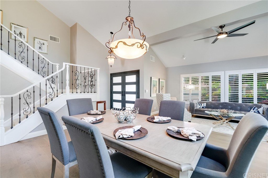 Dining area with large table, gray chairs, chandelier, living room, couch, and stairs.