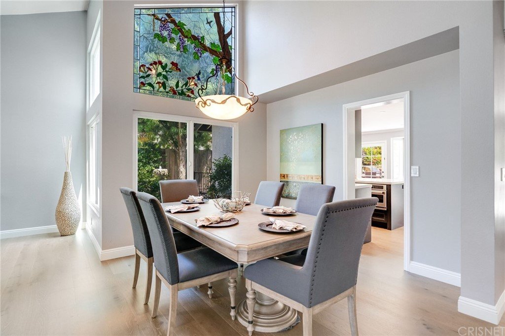 Dining room with large table, upholstered chairs, stained glass window, vase, and doorway.