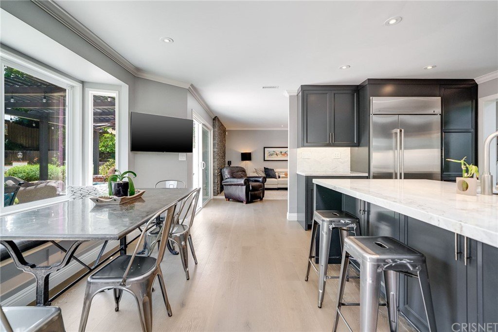 Kitchen with gray cabinets, dining table, metal chairs, stainless steel appliances, and living area.