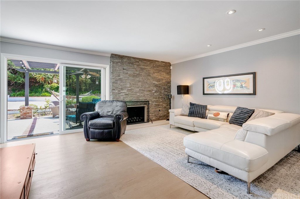 Living room with sectional sofa, chair, stone fireplace, glass doors to patio, wood floor, and rug.