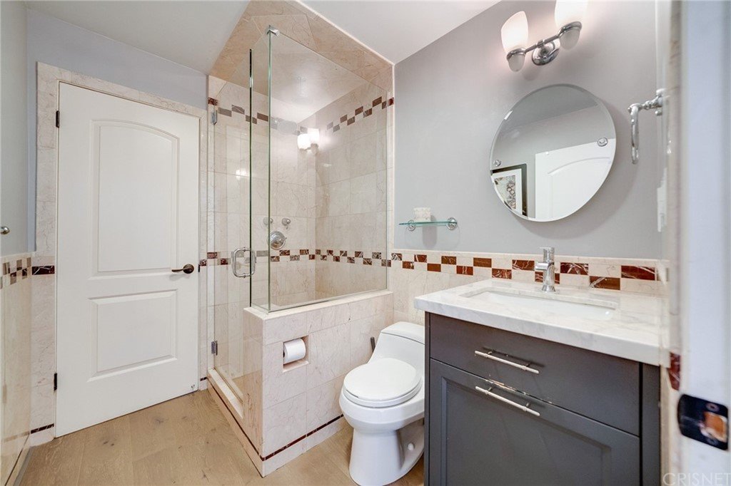 Bathroom with glass shower, toilet, sink vanity, and beige tiles.