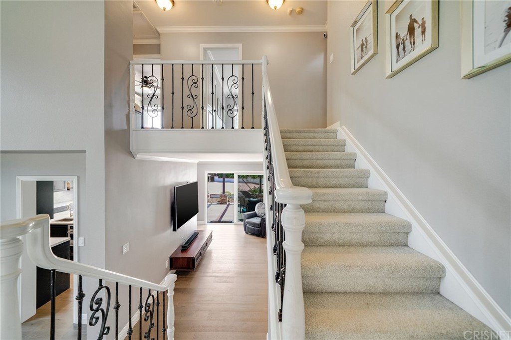 Stairs with iron railing, light carpet, TV on wall, and large windows.