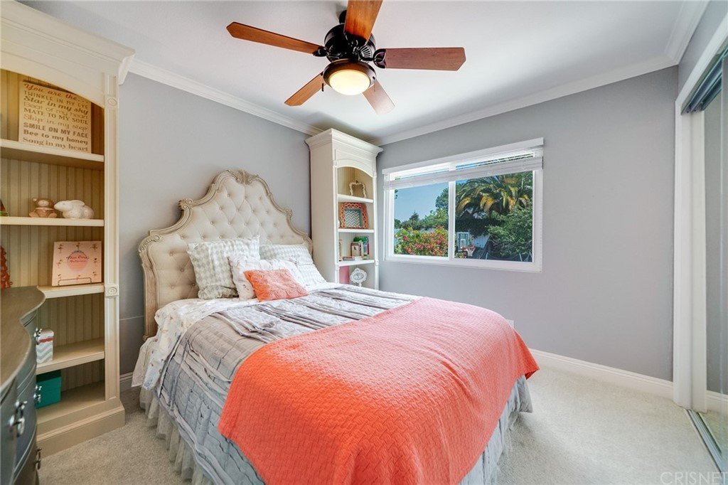 Bedroom with bed, quilt, nightstand, ceiling fan, window, and green view.