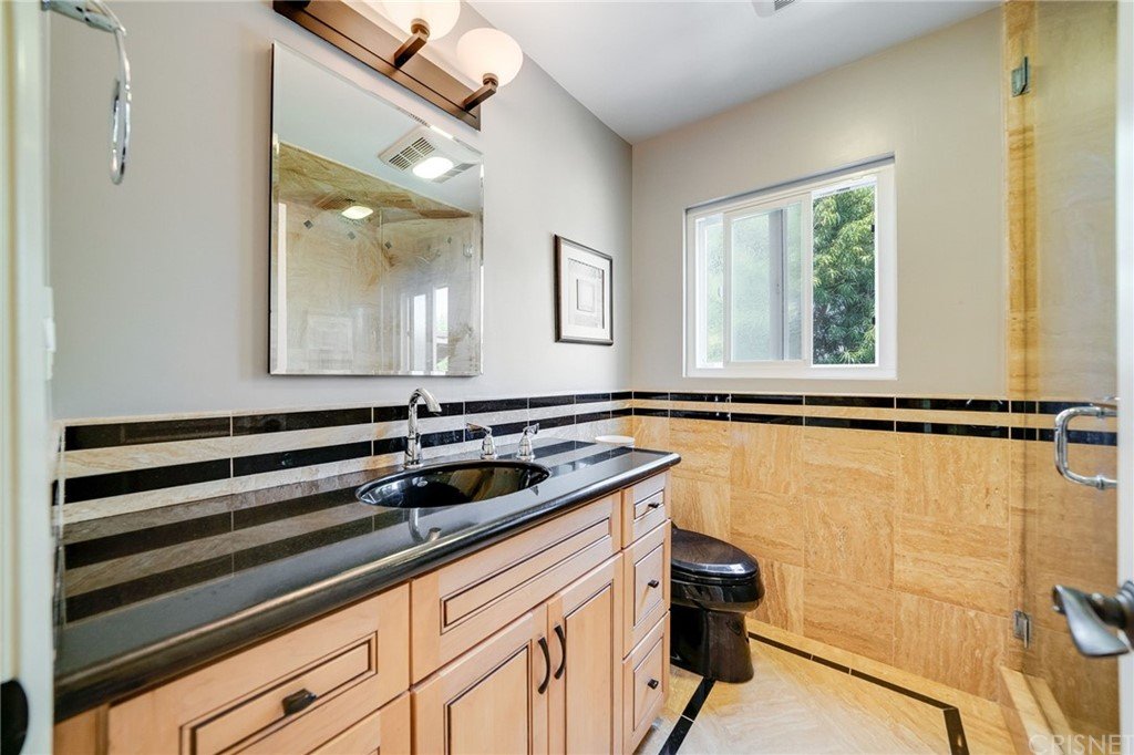 Bathroom with double sinks, black counter, mirror, wood cabinets, toilet, and window.