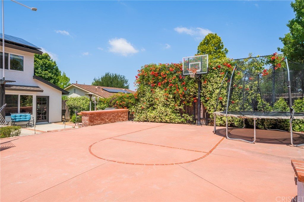California real estate house basketball court with hoop, trampoline, greenery, and nearby homes.
