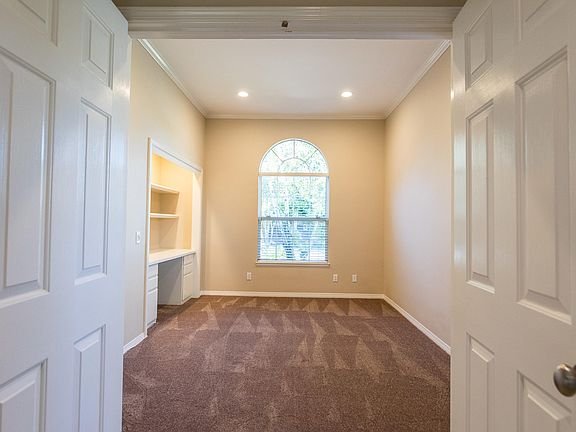Empty room with carpet floor, large arched window, and built-in shelves
