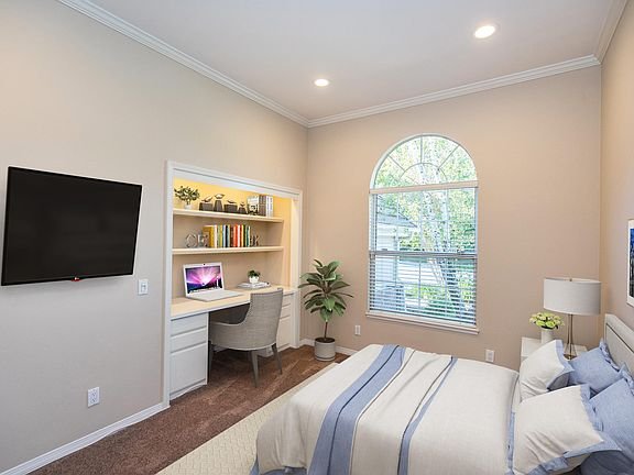 Bedroom with blue and white bed, desk with computer, TV, and plant
