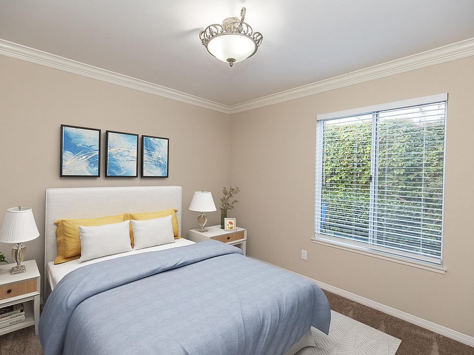 Bedroom with blue bedspread, white pillows, bedside lamps, and wall art