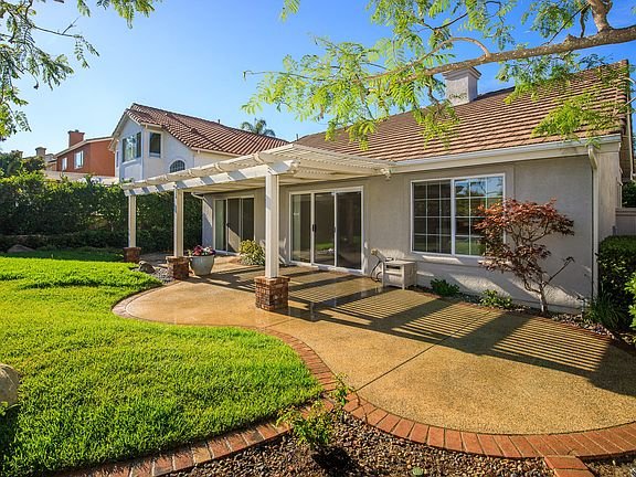 California real estate house with patio, green lawn, large windows, sloped roof, and trees.