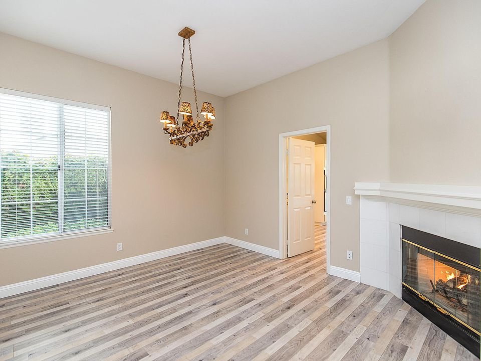 Empty living room with hardwood floor, chandelier, window with blinds, and fireplace