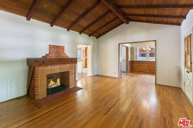 Living room with brick fireplace, wood beams, and wood floor