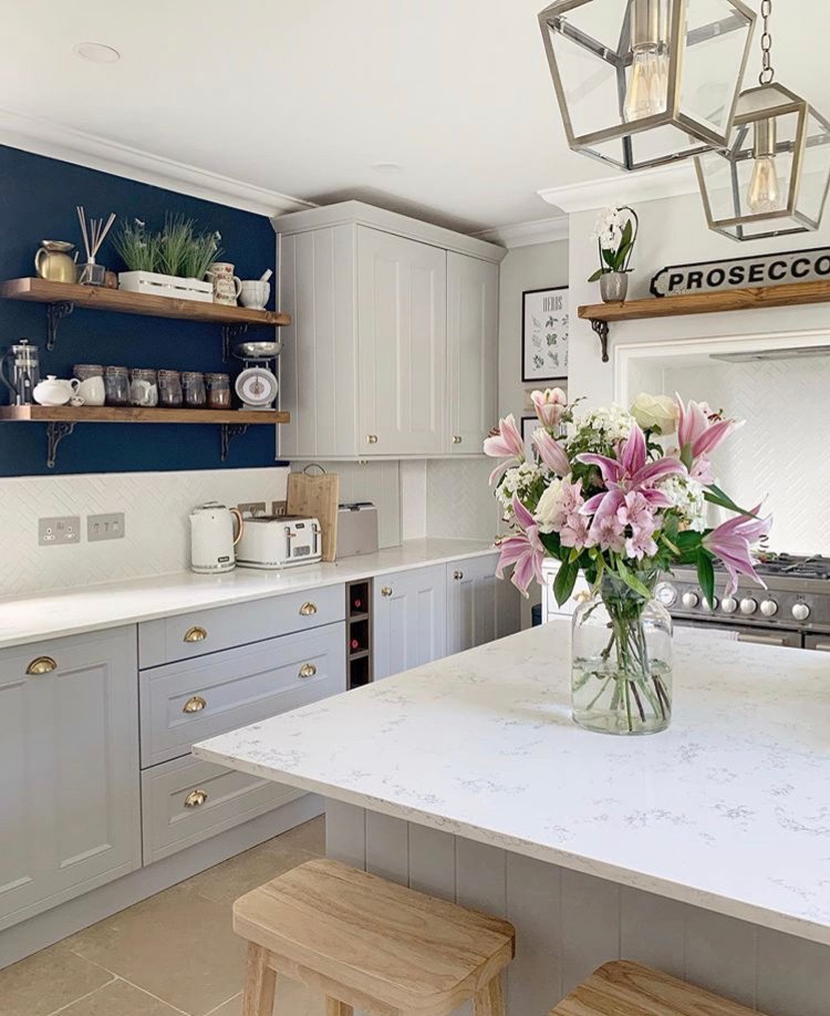 Kitchen with grey cabinets, marble counter, shelves, oven, and pink lilies.