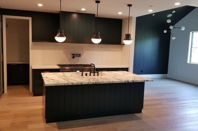 Kitchen with dark cabinets, marble island, and pendant lights.