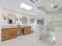 Modern bathroom with double vanity, wood cabinets, two mirrors, and glass shower.