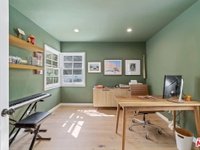 Minimal home office with green walls, wooden desk, keyboard, wall frames, and window.