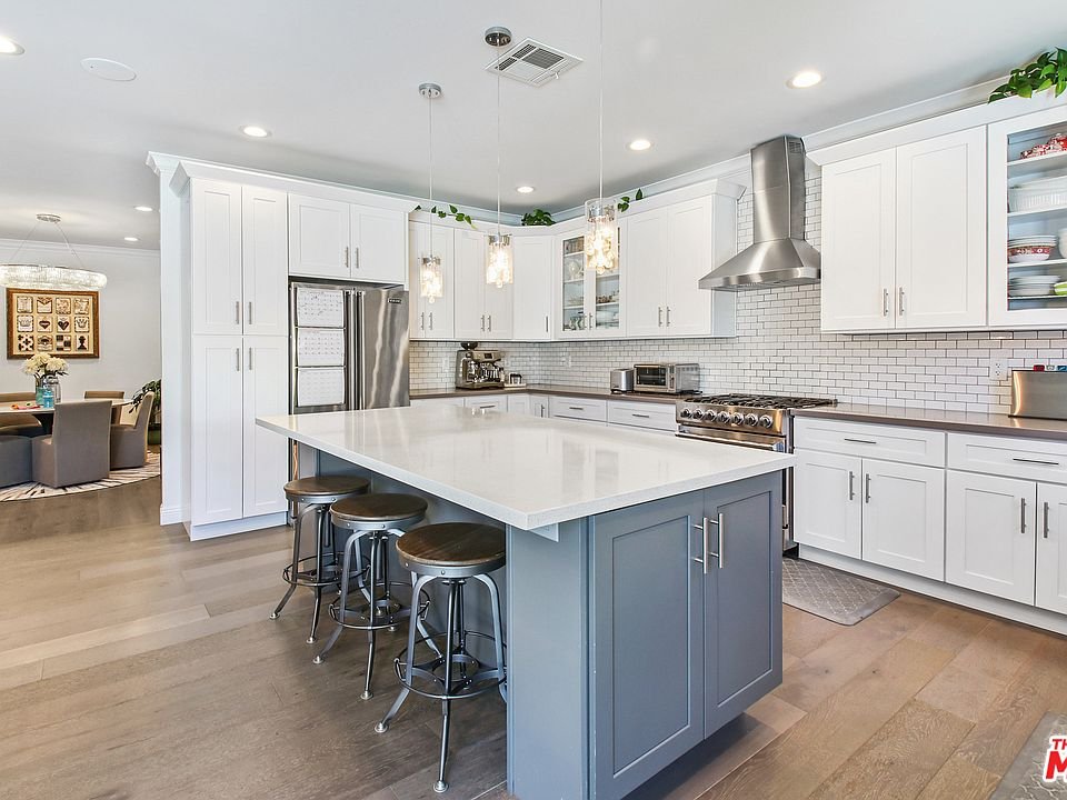 Kitchen with white cabinets, stainless steel appliances, island with stools, and wood floor.