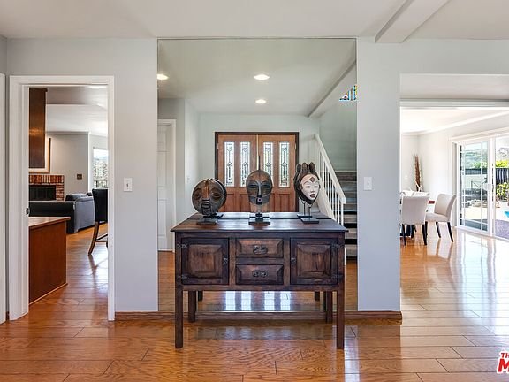 Hallway with wood table, decorative masks, entrance door, and open spaces on both sides.