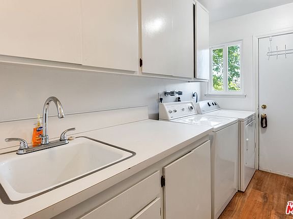 Laundry room with sink, white cabinets, washer, dryer, window, and door outside.