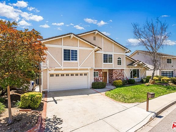 Two story house with light exterior, front lawn, double garage, trees, and shrubs California real estate.